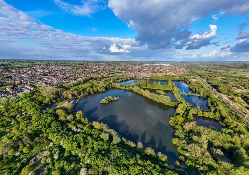 Stunning aerial shot of lakes surrounded by greenery, featuring nearby railway lines under a dramatic sky.